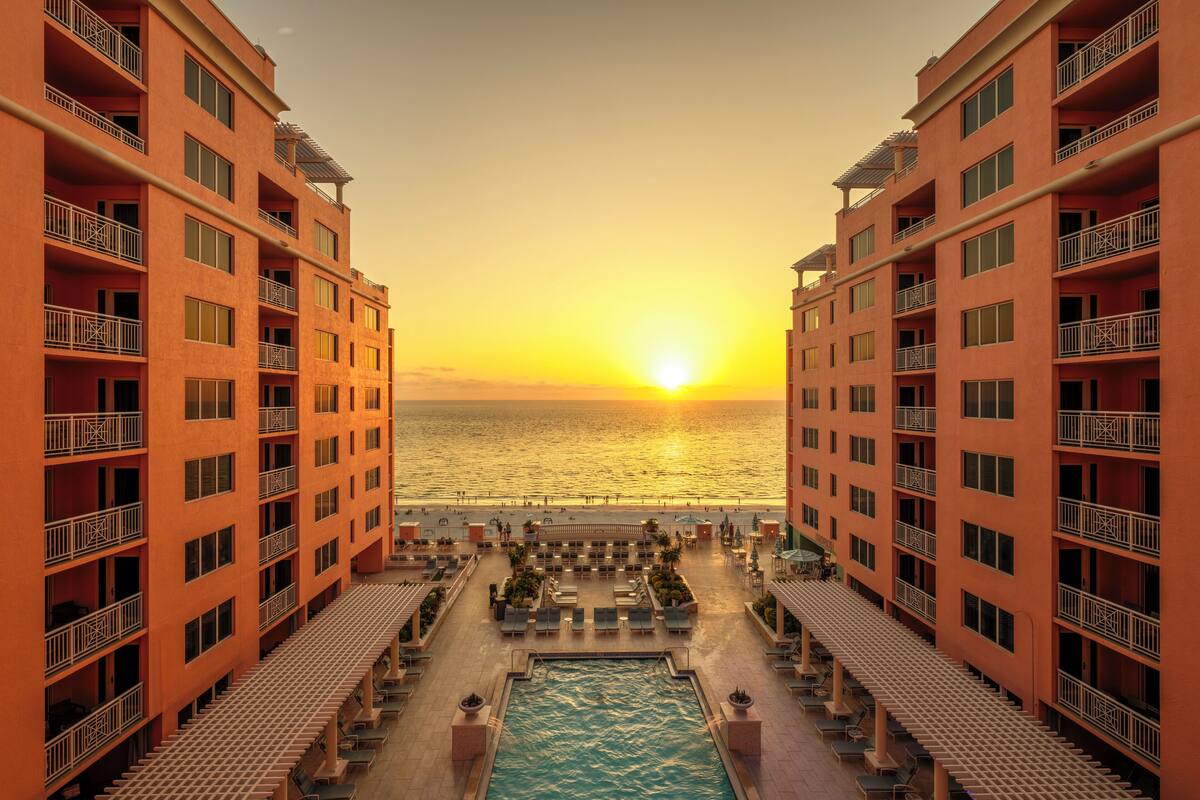 A hotel with a pool, sunbathing areas, and a view of the ocean at sunset.