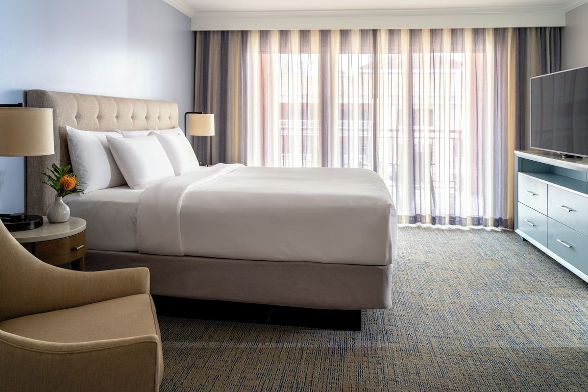 A hotel room with a large bed, a TV, a desk with a lamp, and a chair.