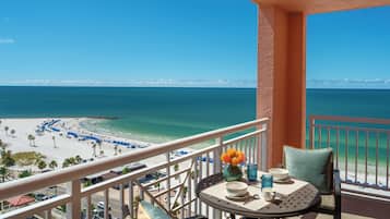 A balcony with a view of the beach and ocean, a table with chairs, and a vase with flowers.