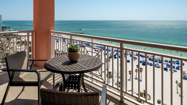 A balcony with a table and chairs, overlooking a beach with blue umbrellas and a clear view of the ocean. - Hyatt Regency Clearwater Beach Resort and Suites (Clearwater Beach)