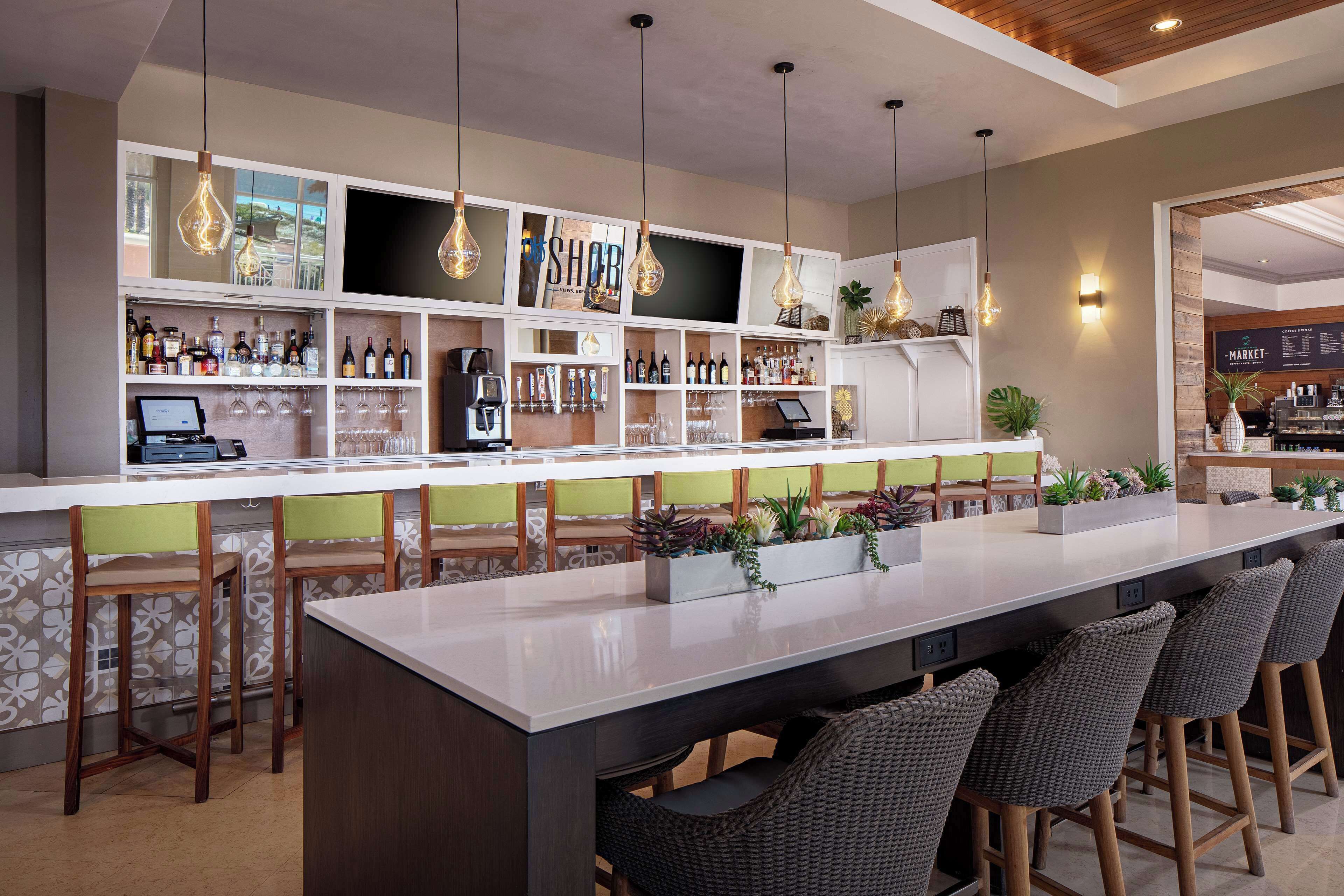 A bar area with a long counter, multiple stools, and shelves stocked with bottles and glasses.