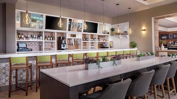 A bar area with a long counter, multiple stools, and shelves stocked with bottles and glasses.