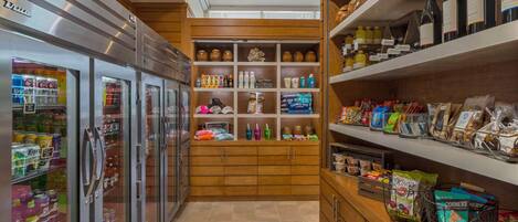 A well-stocked kitchenette with a refrigerator, shelves with beverages, snacks, and a coffee machine.