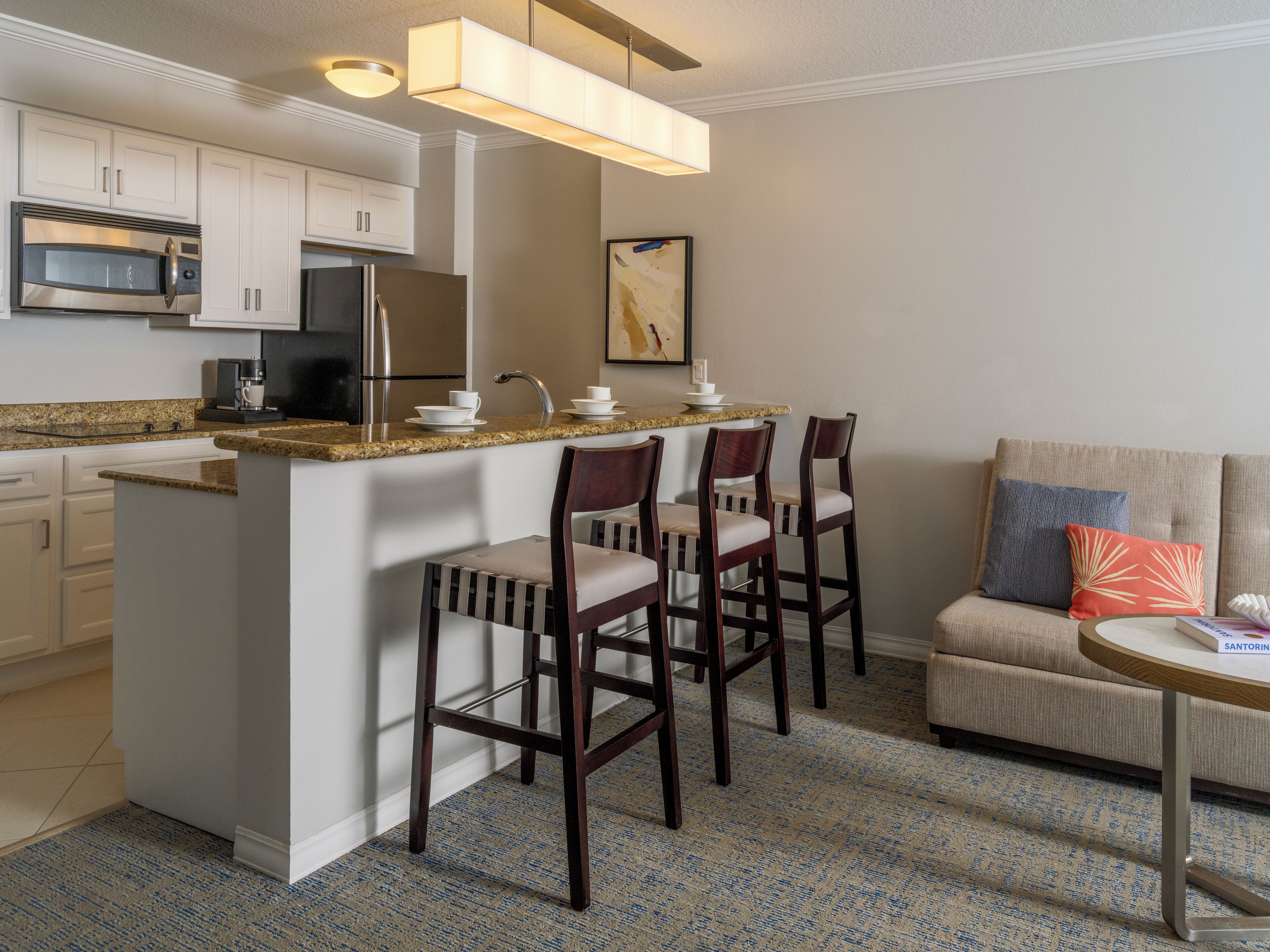 A compact kitchen with a central island, bar stools, a coffee machine, and a refrigerator.