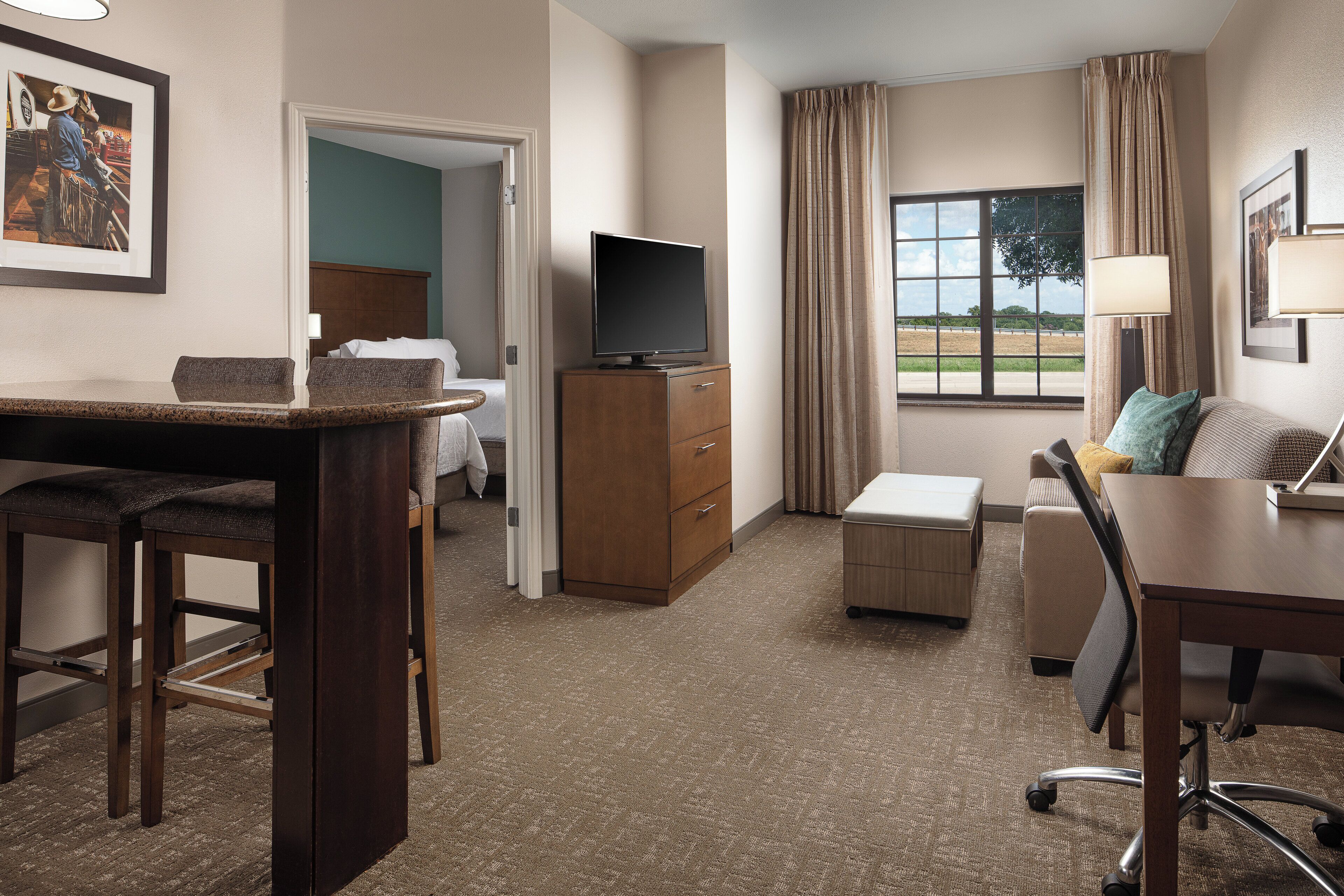 Une chambre d’hôtel avec un lit, un bureau et une chaise, une télévision et une fenêtre avec des rideaux.