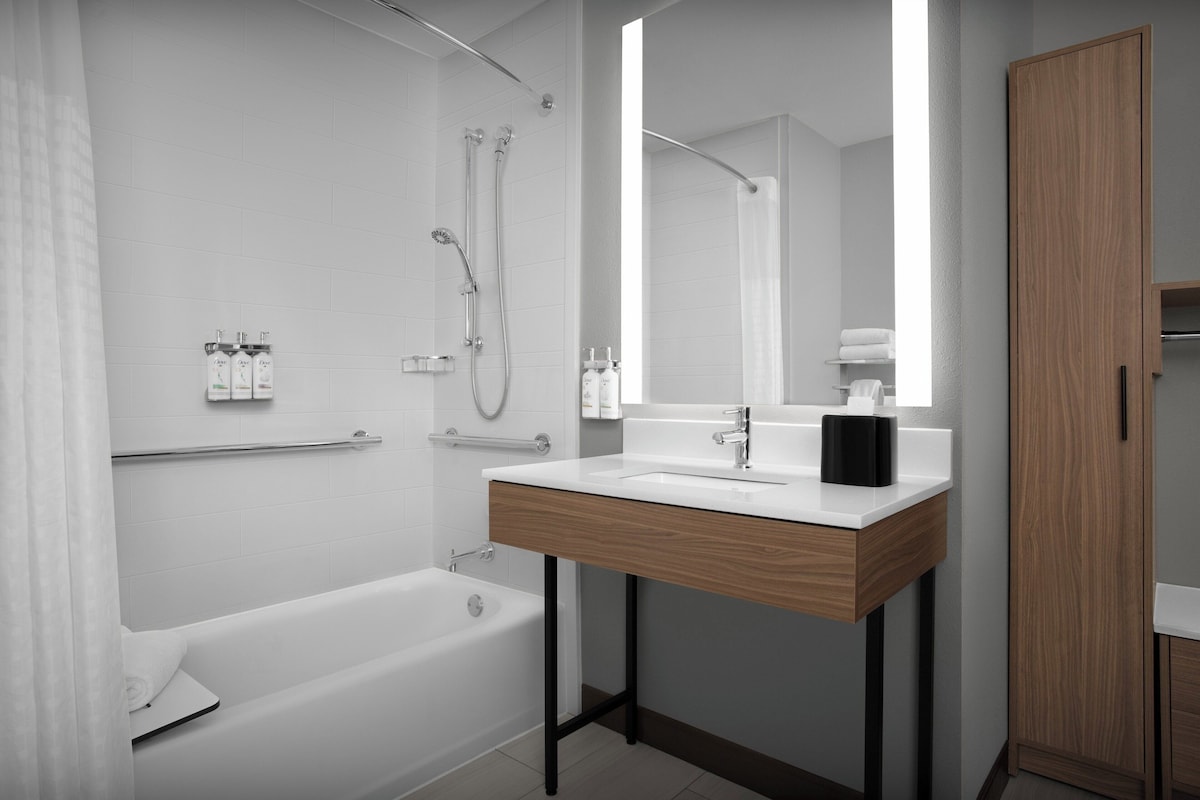 A modern bathroom with a bathtub, a wooden vanity with a sink, and a large mirror.