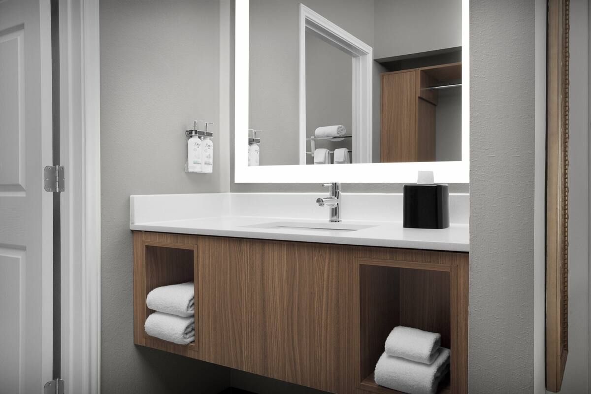 Une salle de bain moderne avec un lavabo blanc, un grand miroir et des meubles en bois.