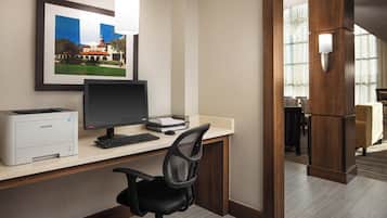 A hotel office with a desk, computer, printer, and framed picture.