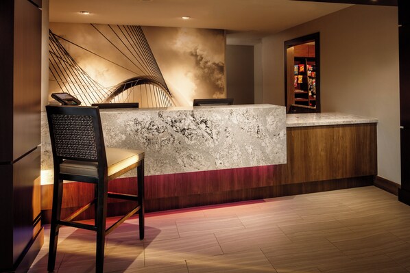 A modern reception desk with a marble top, a wooden counter, and a seating area with a chair.