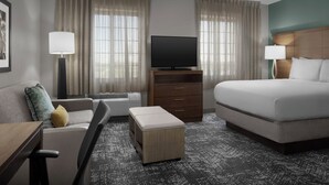 A hotel room with a bed, a TV on a stand, a sofa, a desk, and a window with curtains.