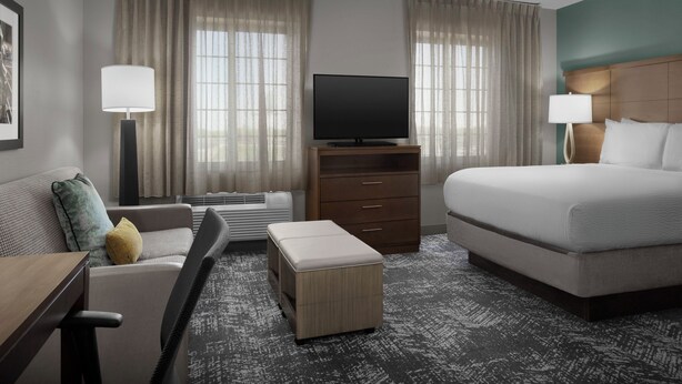 A hotel room with a bed, a TV on a stand, a sofa, a desk, and a window with curtains.