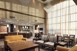 A hotel lobby with a reception desk, seating area, and large windows.