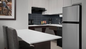 A modern kitchen with white cabinets, a stainless steel refrigerator, a coffee maker, and a framed picture on the wall.