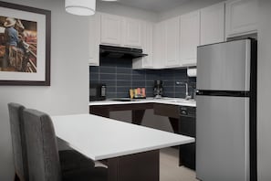 A modern kitchen with white cabinets, a stainless steel refrigerator, a coffee maker, and a framed picture on the wall.