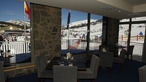 A restaurant with a stone wall and large windows overlooking a snowy ski slope.