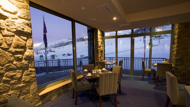 A dining area with a table set for four, large windows offering a view of a snowy landscape, stone walls, and a balcony with a railing.