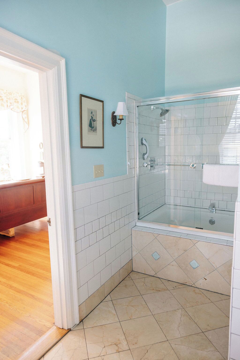 Un baño con ducha envuelta en vidrio, paredes de azulejos blancos y suelo de madera.