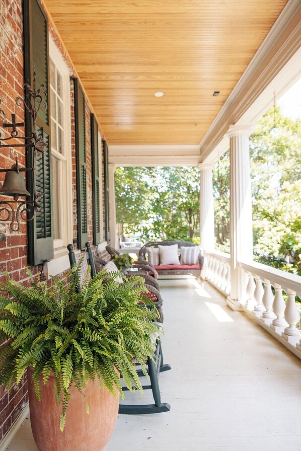 A covered porch with a brick wall, a wooden ceiling, and a seating area with a sofa and chairs.