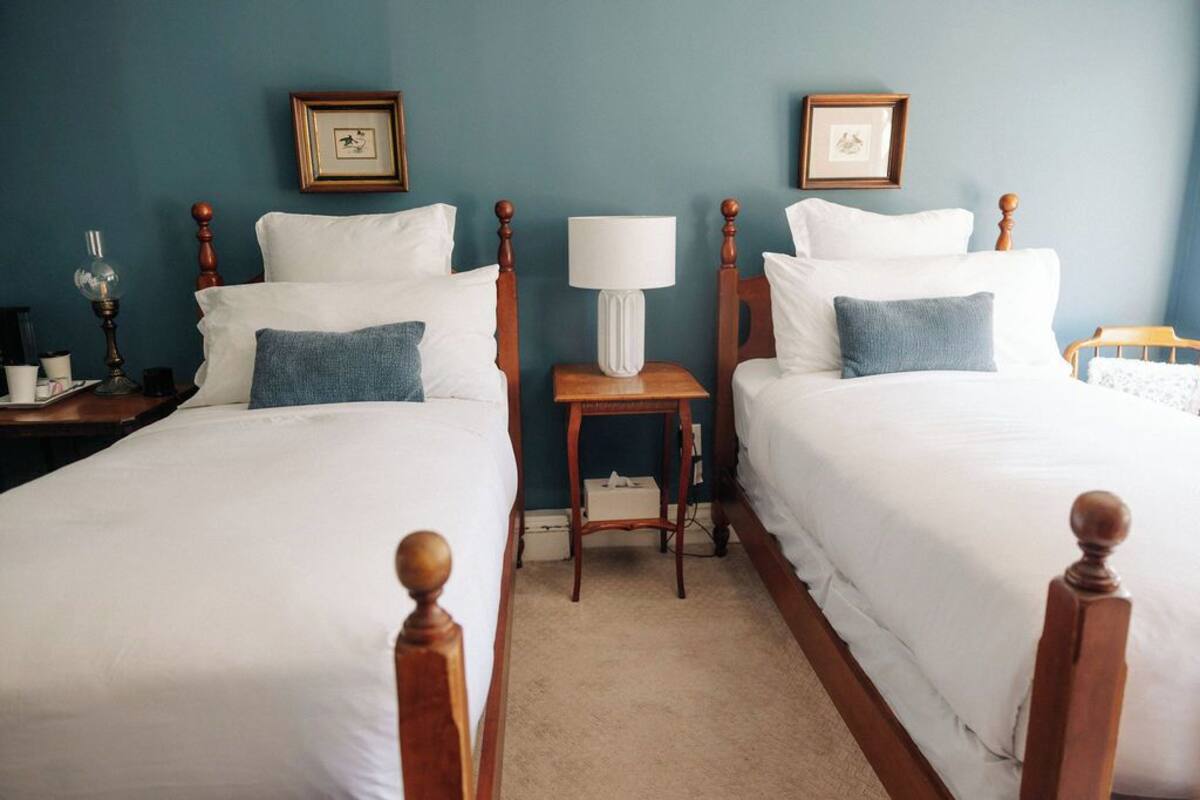 A room with two single beds, a nightstand with a lamp, and framed pictures on the wall.
