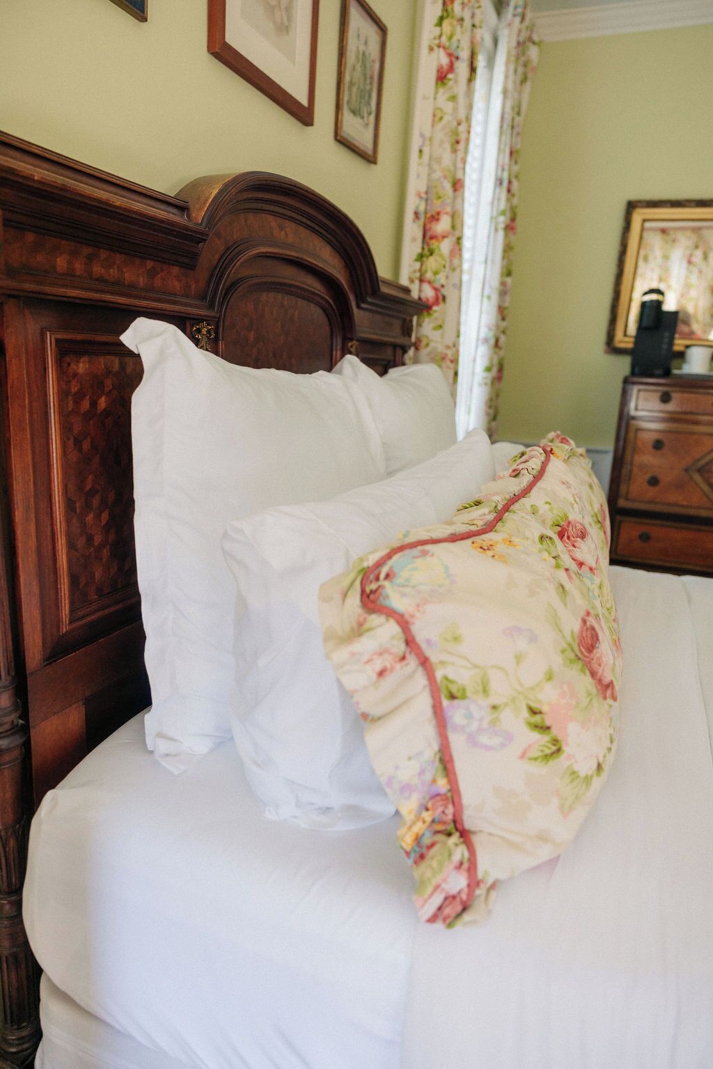 A bed with a floral-patterned blanket and white pillows in a room with a wooden headboard and floral curtains.