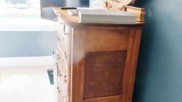 A wooden dresser with a mirror and a laptop in a room with blue walls and a window.