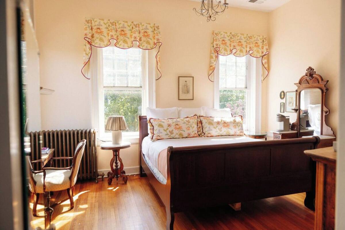 A bedroom with a wooden bed, a chair, a table, and a radiator.