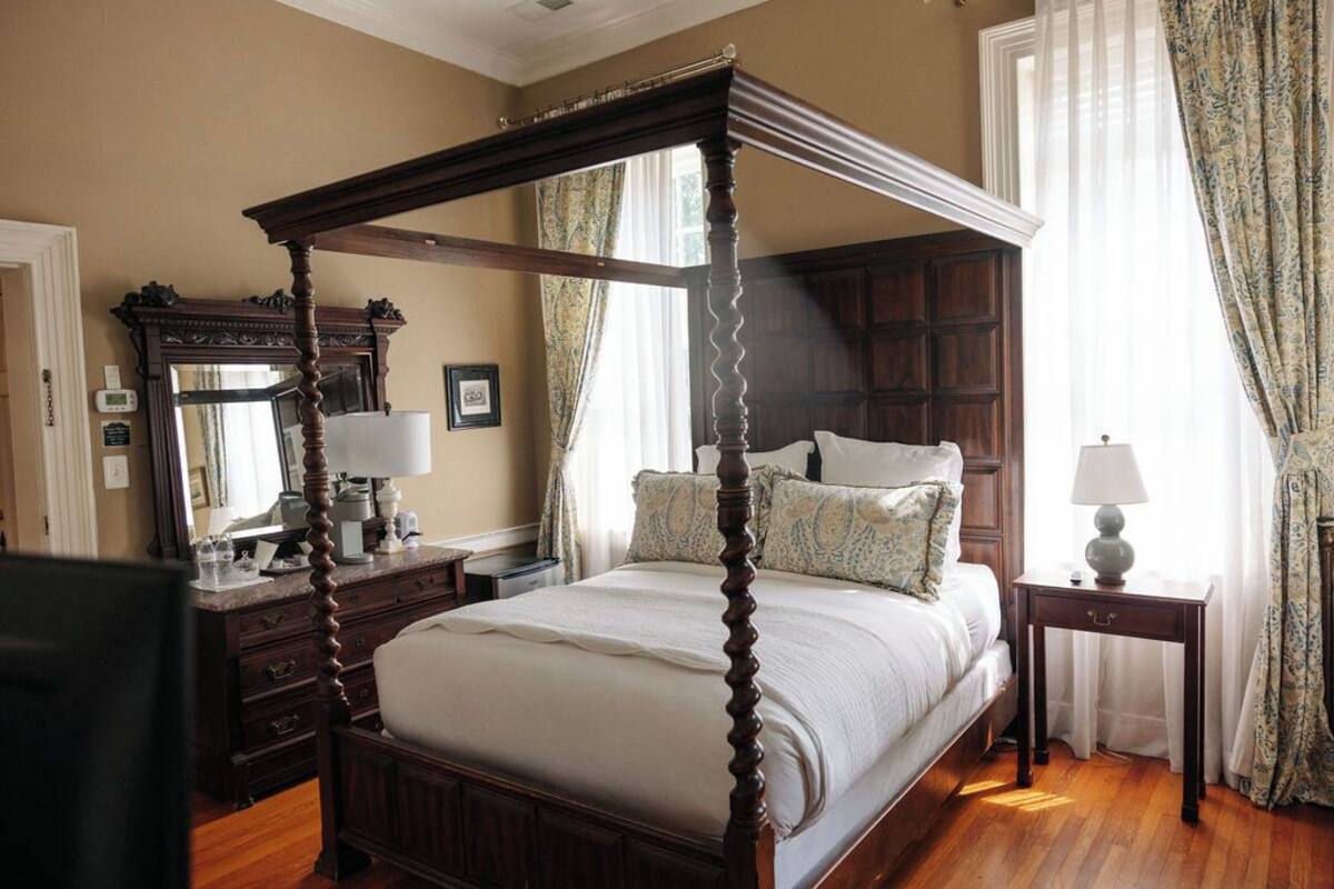 A four-poster bed with a wooden frame, a bedside table with a lamp, and a dresser with a mirror.