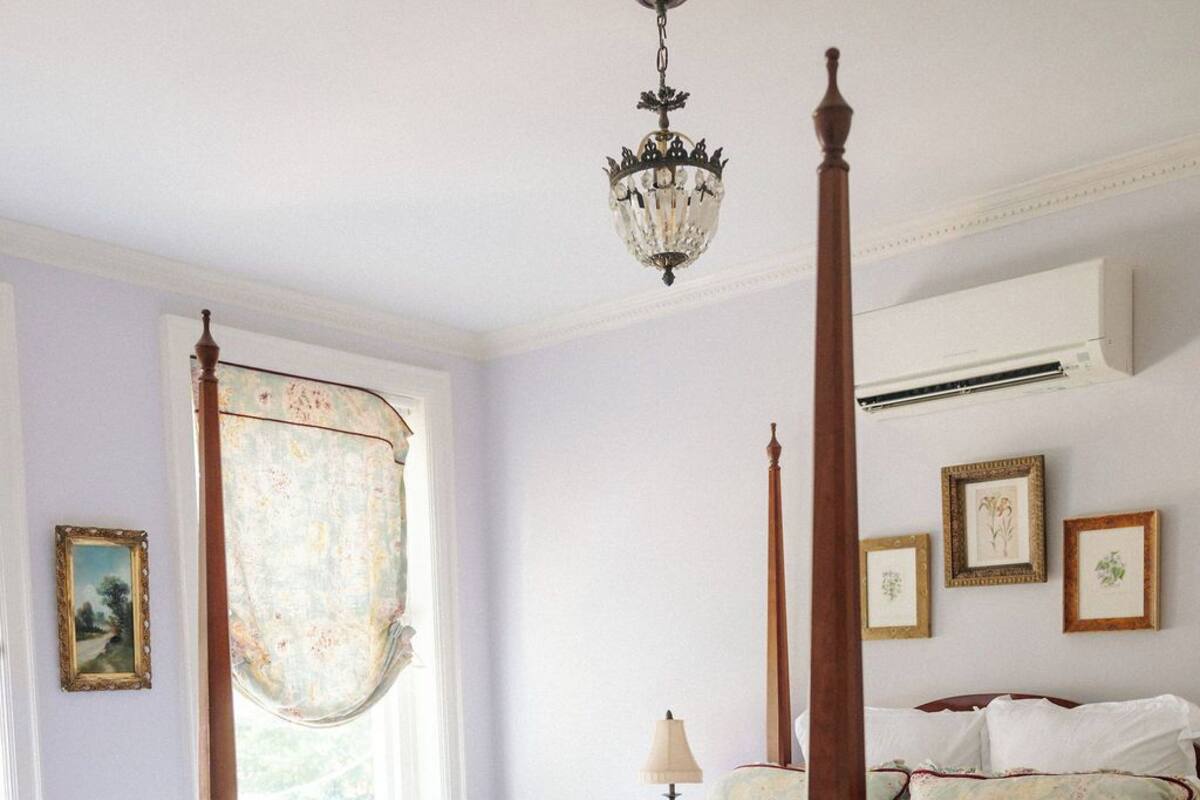 A four-poster bed with a canopy, a bedside table, a lamp, and framed botanical prints on the wall.