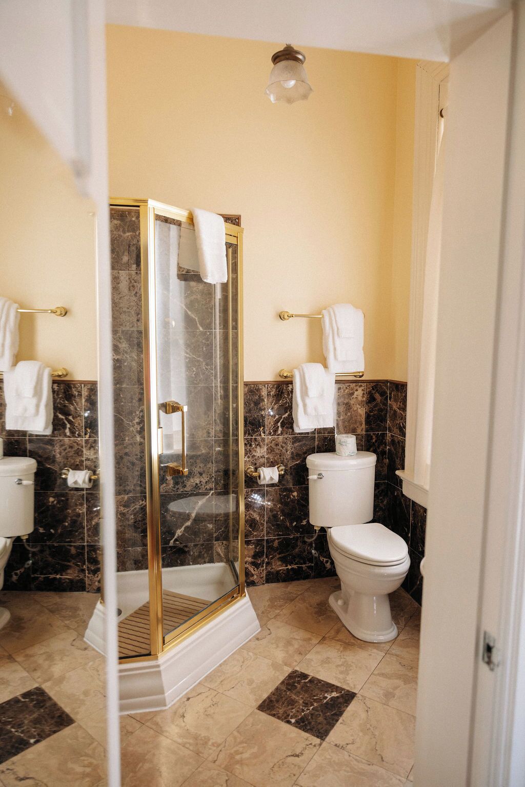 Un baño con ducha separada por mampara de vidrio, baldosas de mármol y dos inodoros.