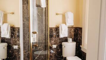 Un baño con ducha separada por mampara de vidrio, baldosas de mármol y dos inodoros.