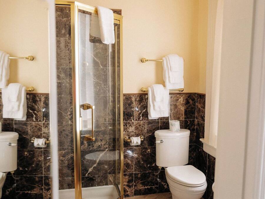 Un baño con ducha separada por mampara de vidrio, baldosas de mármol y dos inodoros.