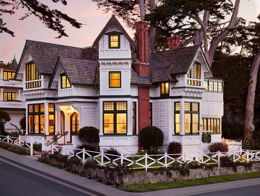 A large, multi-story house with a prominent chimney, multiple windows, and a white picket fence.