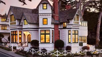 A large, multi-story house with a prominent chimney, multiple windows, and a white picket fence.