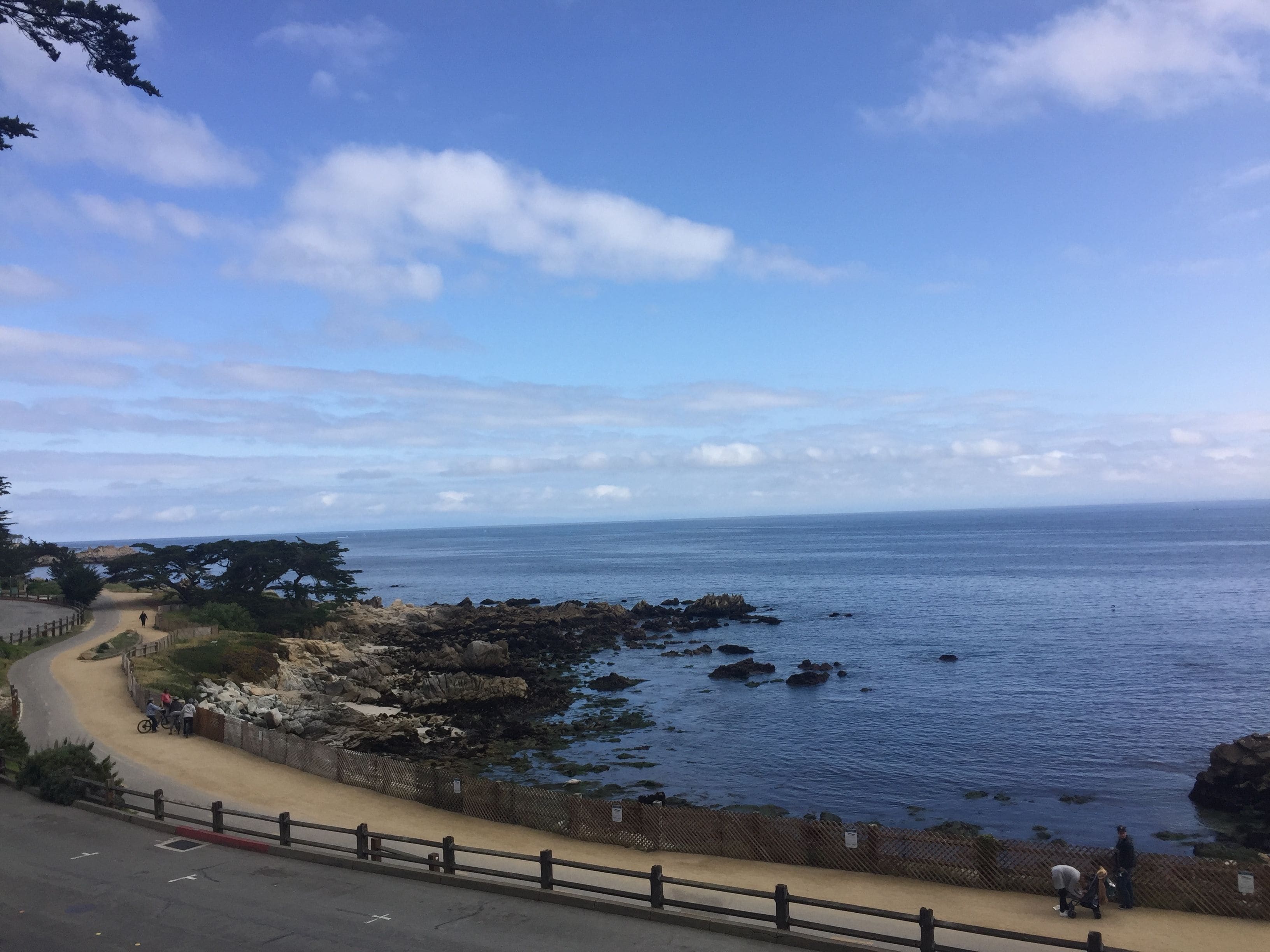 A coastal road with a paved path, rocky shoreline, and a clear view of the sea.