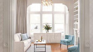 A spacious room with a large window, a white sofa, a blue armchair, and a coffee table. - Green Gables Inn, A Four Sisters Inn (Pacific Grove)