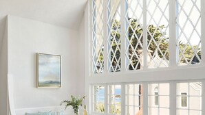A bright room with a white bench, ottomans, and a window with lattice. - Green Gables Inn, A Four Sisters Inn (Pacific Grove)
