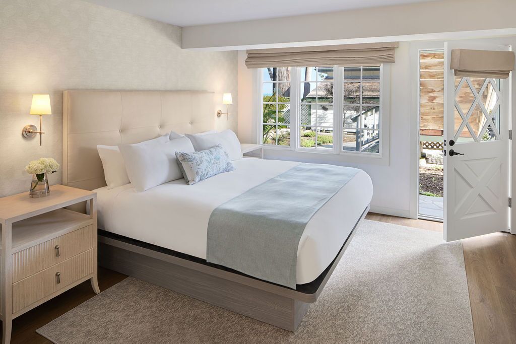 Un dormitorio con una cama grande, mesitas de noche, una mesita auxiliar, una ventana con vistas y una puerta que da al exterior.