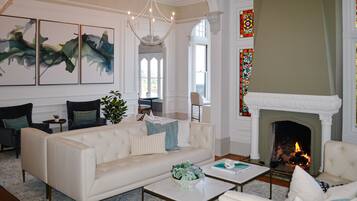 A spacious living room with a white fireplace, comfortable seating, and large windows.