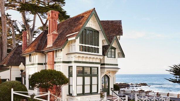 A coastal house with a prominent bay window, a stone foundation, and a view of the ocean. - Green Gables Inn, A Four Sisters Inn (Pacific Grove)