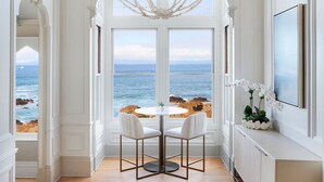 A room with a large window overlooking the sea, a chandelier, and a dining table with chairs. - Green Gables Inn, A Four Sisters Inn (Pacific Grove)
