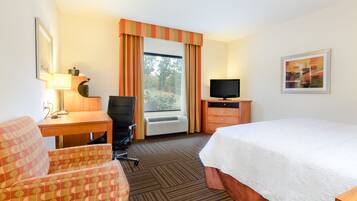 A hotel room with a bed, desk, chair, television, and a window with curtains.