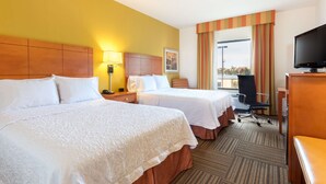 Une chambre d’hôtel avec deux lits, un bureau, une chaise, une télévision et une fenêtre avec des rideaux.