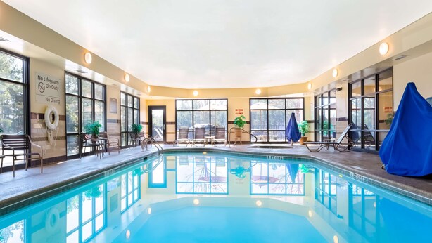 Une piscine intérieure avec des parois en verre transparent, un poste de surveillance pour le sauveteur et un panneau indiquant qu’il est interdit de plonger.