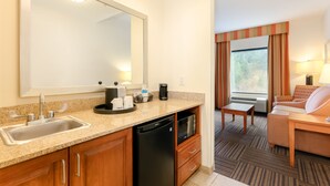 Une chambre d’hôtel avec un coin cuisine comprenant un évier, un four à micro-ondes et une machine à café. On y trouve également une table à manger et un canapé dans l’espace salon.