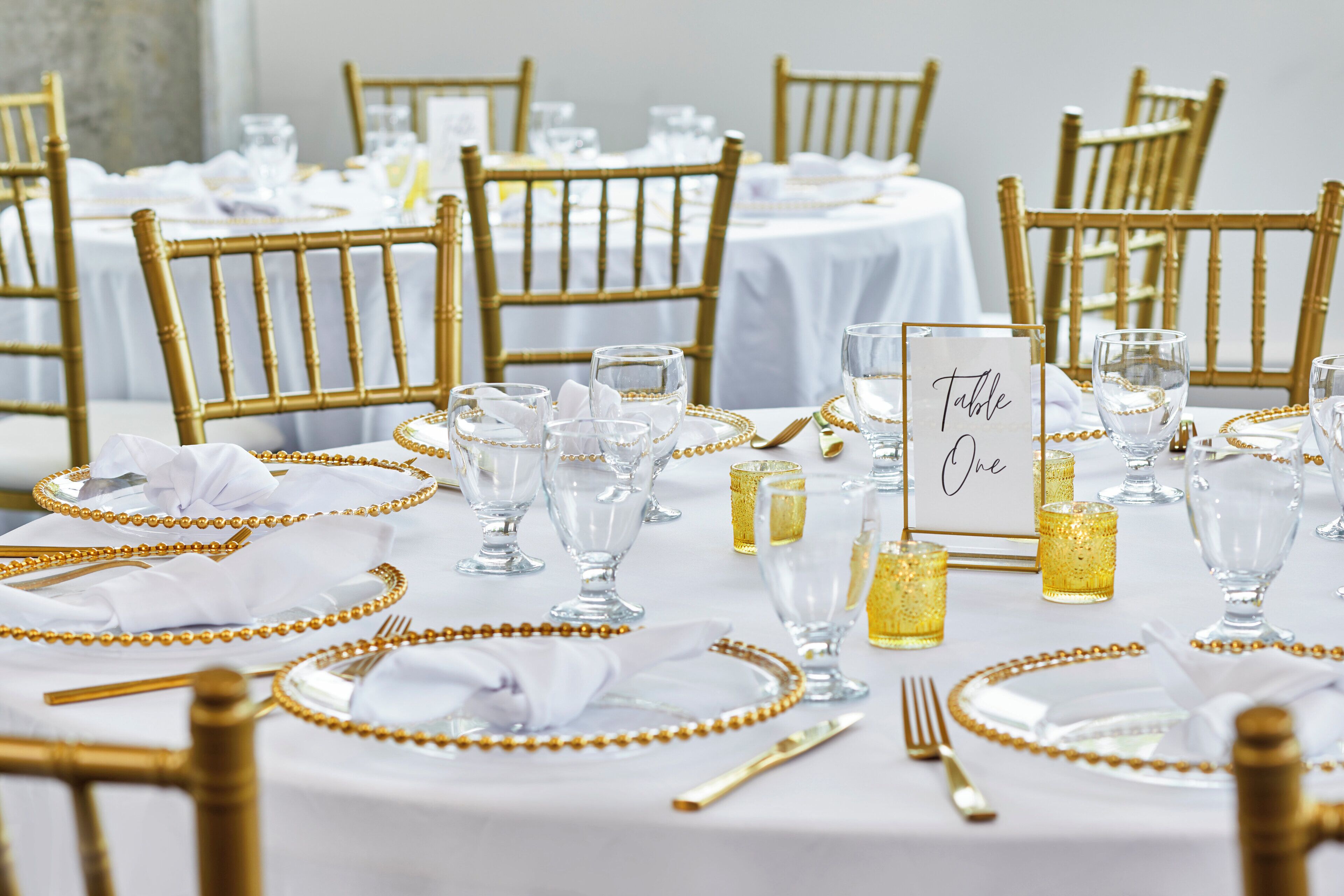 A table set with gold bead accents, clear glassware, and a 'Table One' sign.