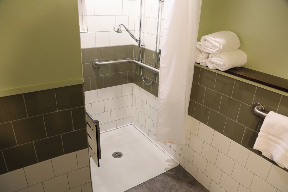 A small, accessible shower area with a grab bar, a white towel on a shelf, and a shower curtain.