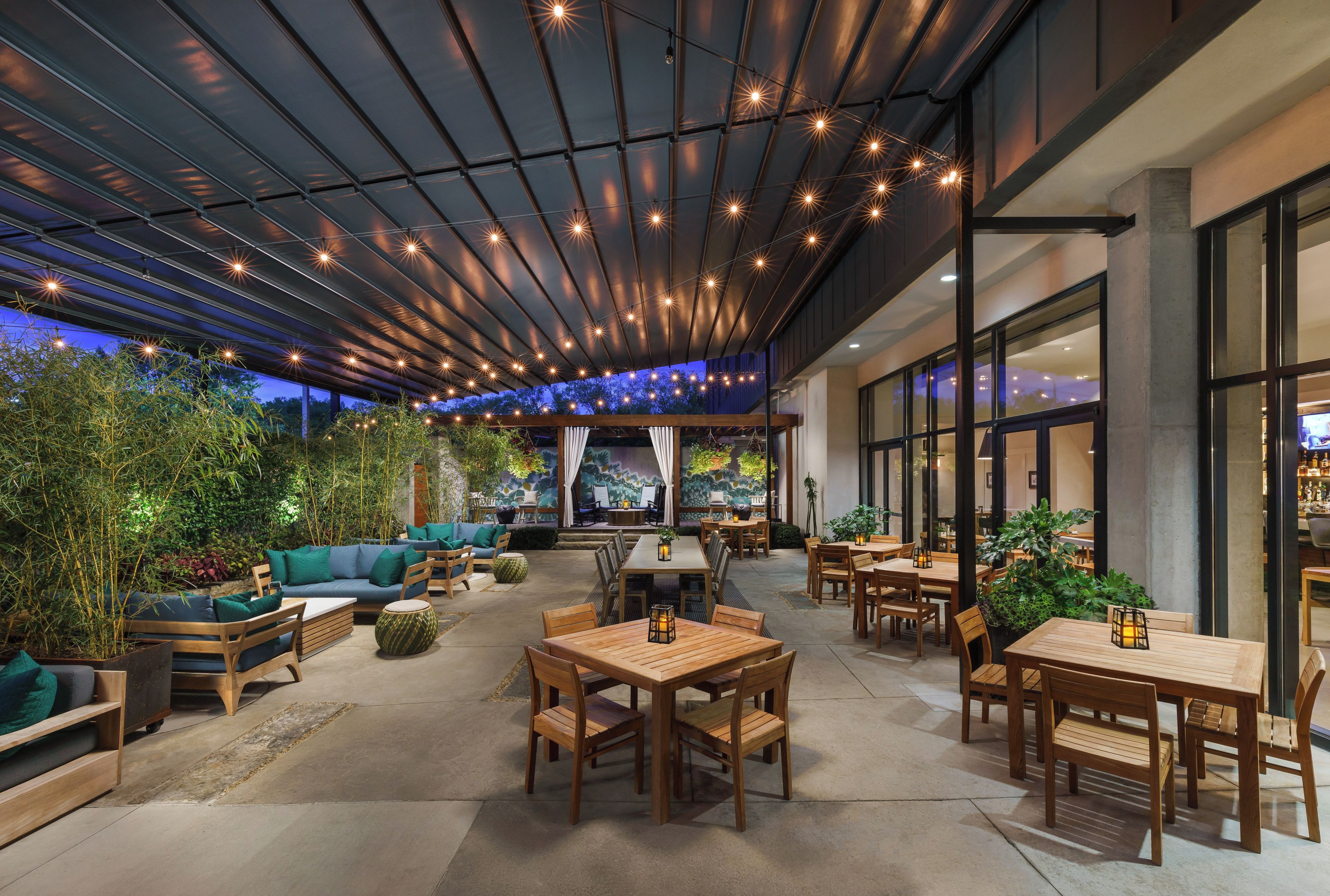 An outdoor seating area with wooden tables and chairs, surrounded by greenery and a view of the cityscape.