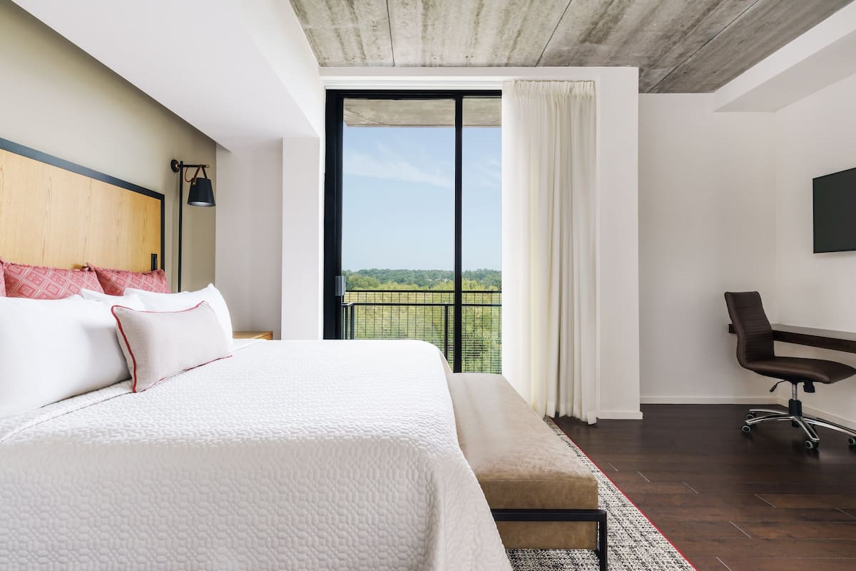 Een moderne hotelkamer met een groot bed, een bureau en uitzicht op een groen landschap door een groot raam.