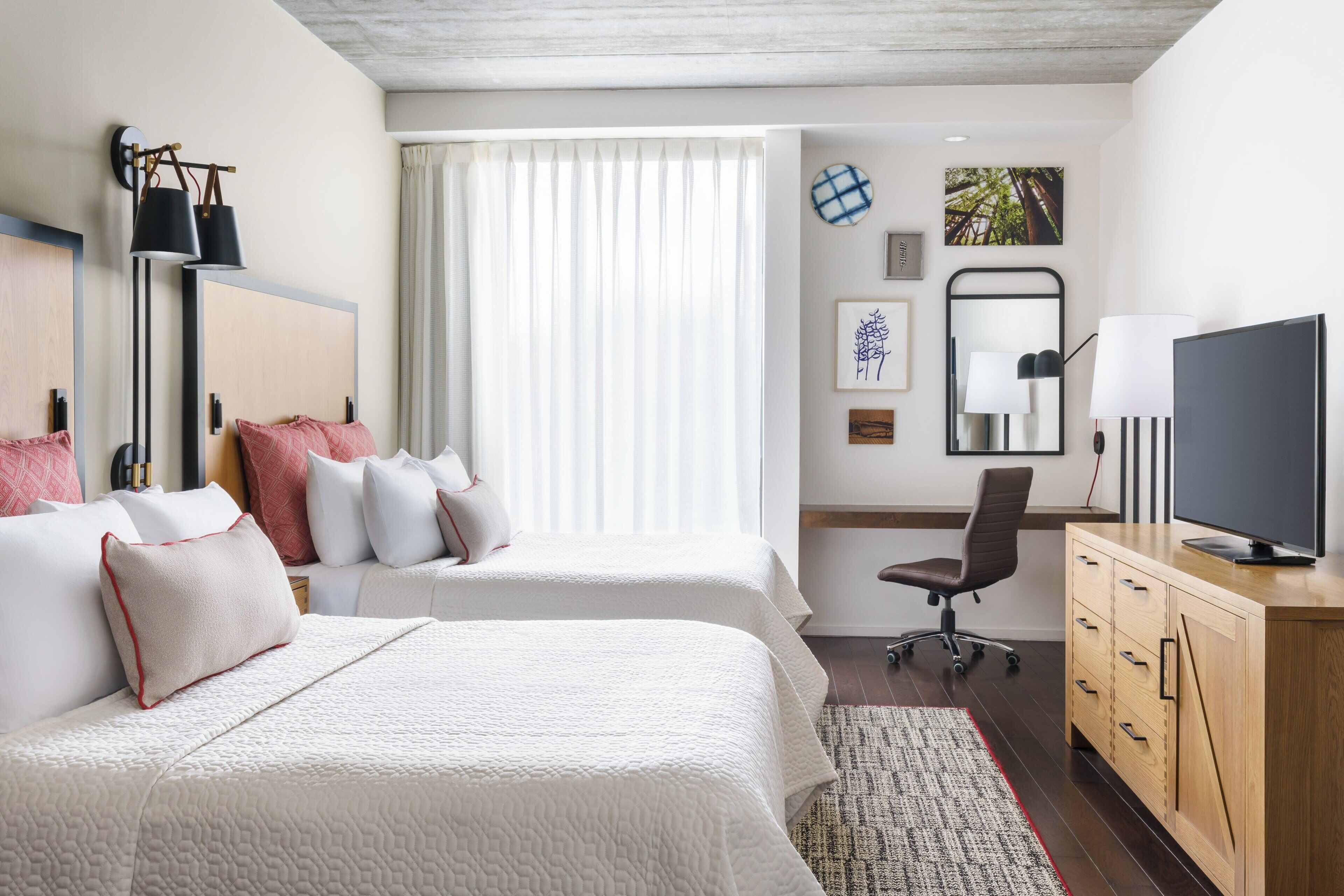 Una habitación de hotel con dos camas, un escritorio, un televisor y una ventana con cortinas.