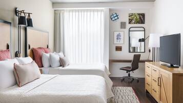 Una habitación de hotel con dos camas, un escritorio, un televisor y una ventana con cortinas.